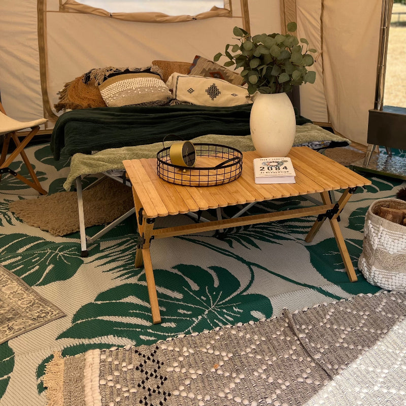 Wooden table with decorative items in a Glawning tent setting with a green leaf-patterned bell tent mat.