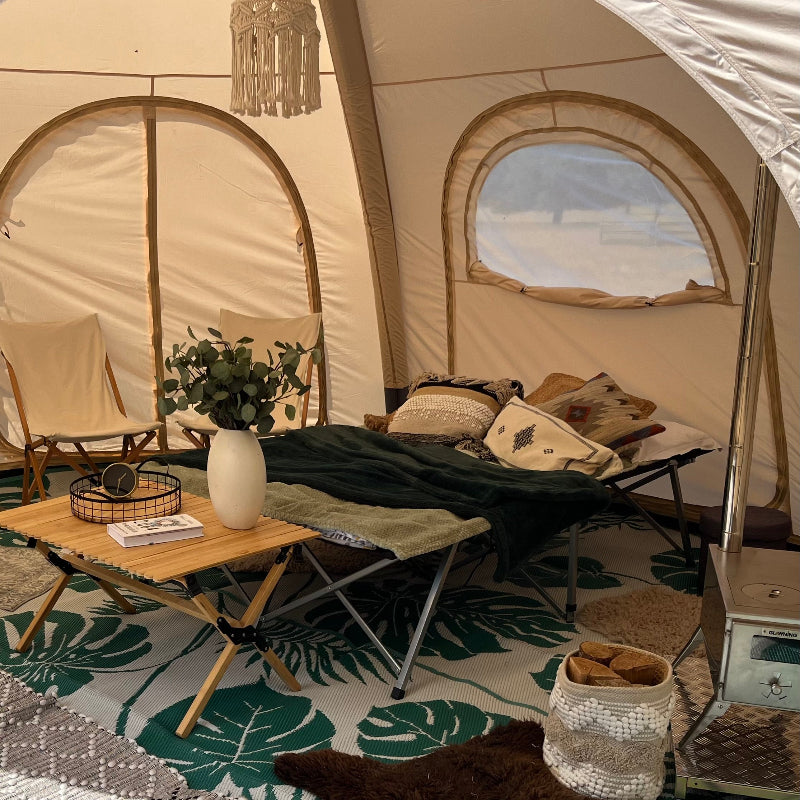 Interior of a 5 metre Glawning AIR tent with furniture and decor, including a table with a plant and books, chairs, and a rug.