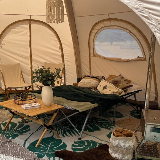 Interior of a 5 metre Glawning AIR tent with furniture and decor, including a table with a plant and books, chairs, and a rug.