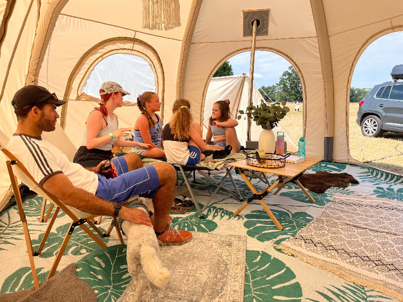 Group of people sitting inside a 5m Glawning AIR tent with a car visible outside.