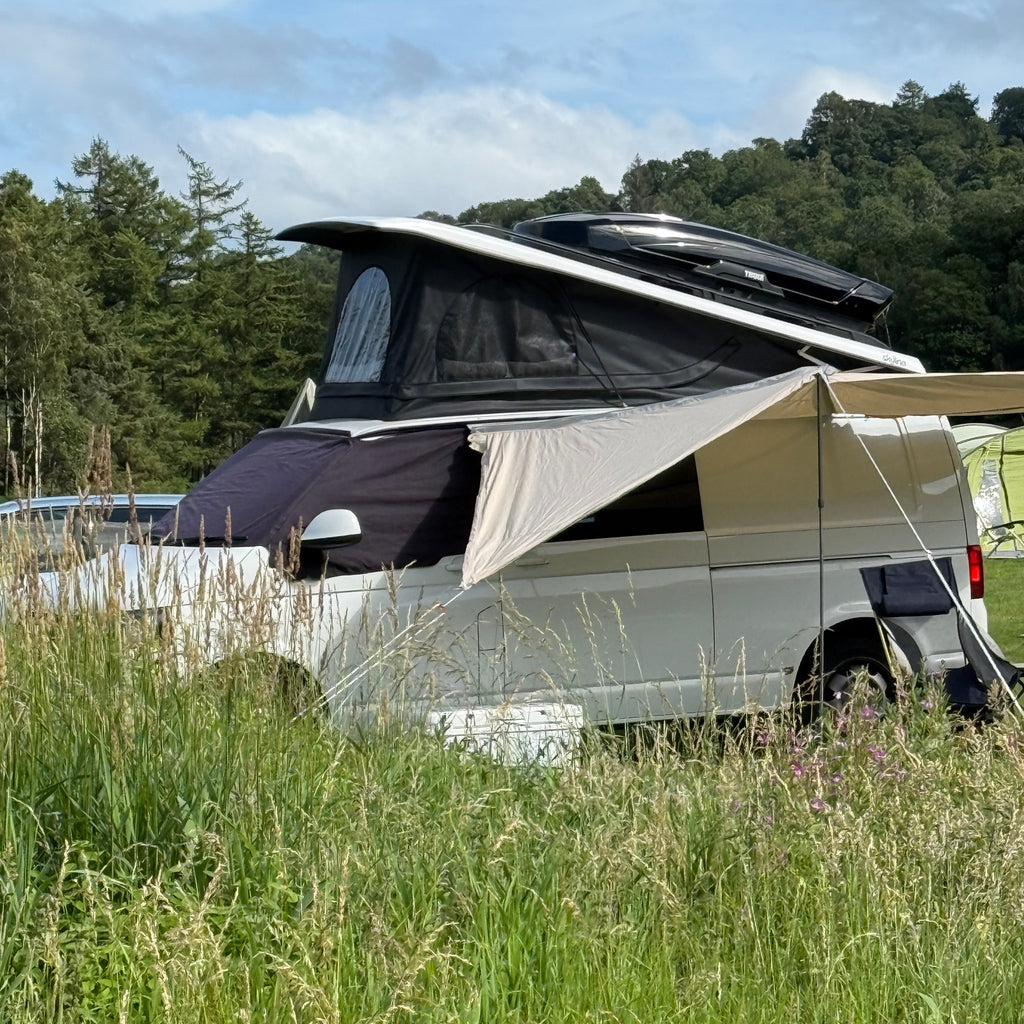 Campervan with a roof box and a Alanopy by Glawning parked on grass next to a body of water with trees in the background