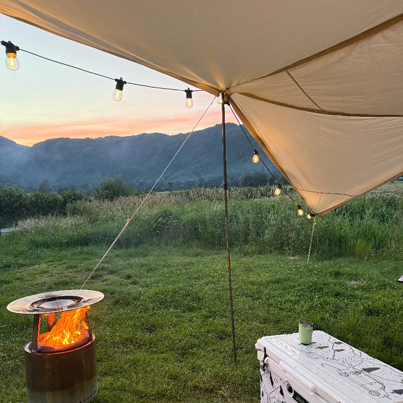 Camping scene with a Glanopy by Glawning, cooler, and fire pit in a grassy area.