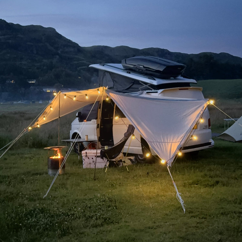 Camping scene with a Glanopy by Glawning, hammock, and vehicle in a mountainous area at dusk.