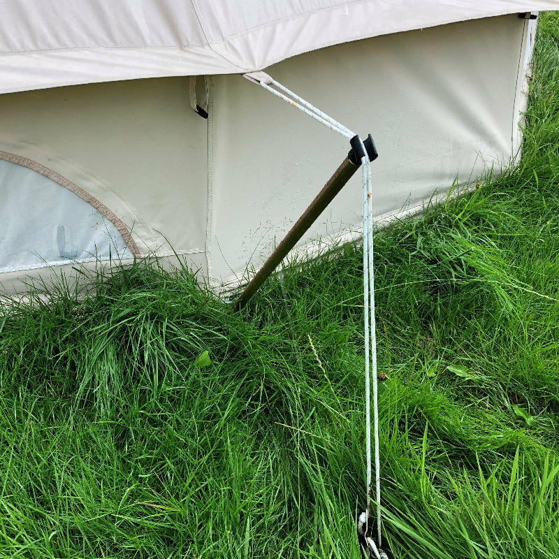 A reducer pole for a bell tent, placed in the grass, with part of a white tent visible in the background.