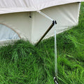 A reducer pole for a bell tent, placed in the grass, with part of a white tent visible in the background.